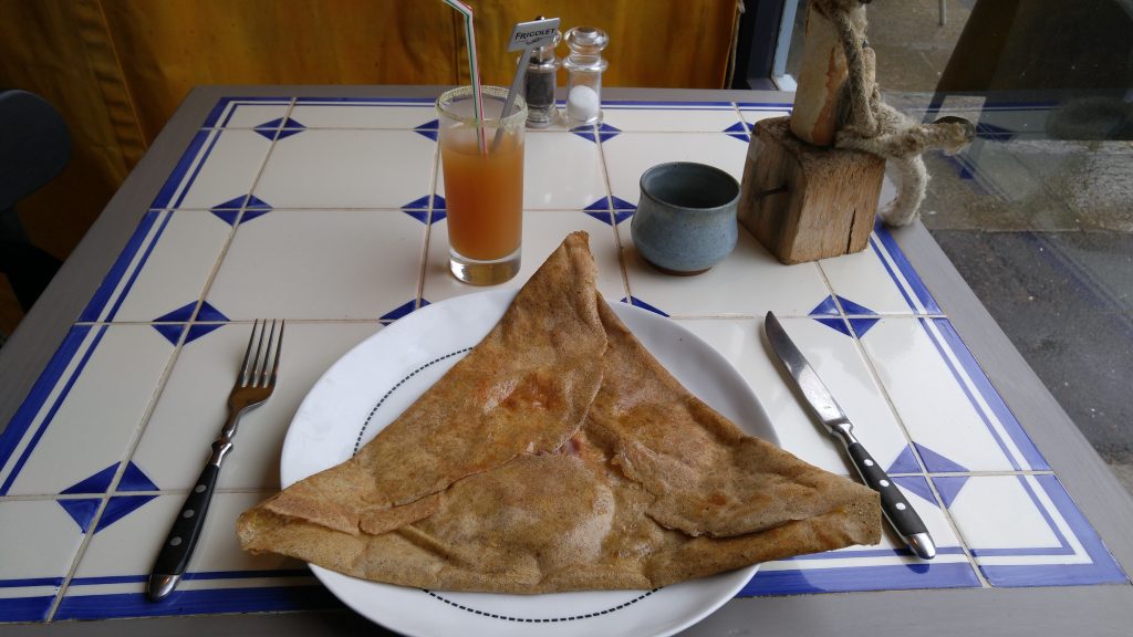 A triangular buckwheat crêpe (galette) sitting on a plate on a restaurant table