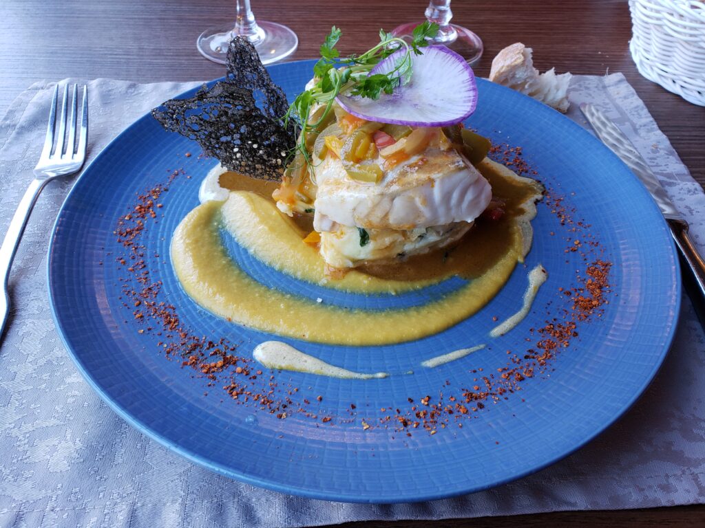 A blue dinner plate with fish over potatoes in the middle surrounded by a swirl of yellow sauce.